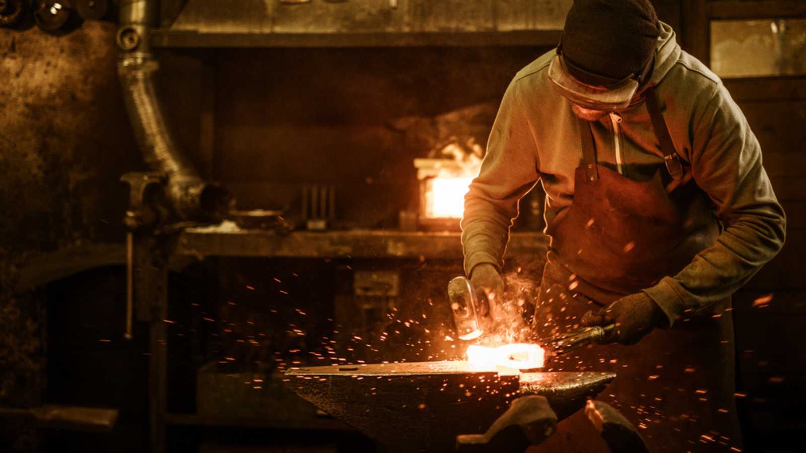 The blacksmith forging the molten metal on the anvil in smithy.