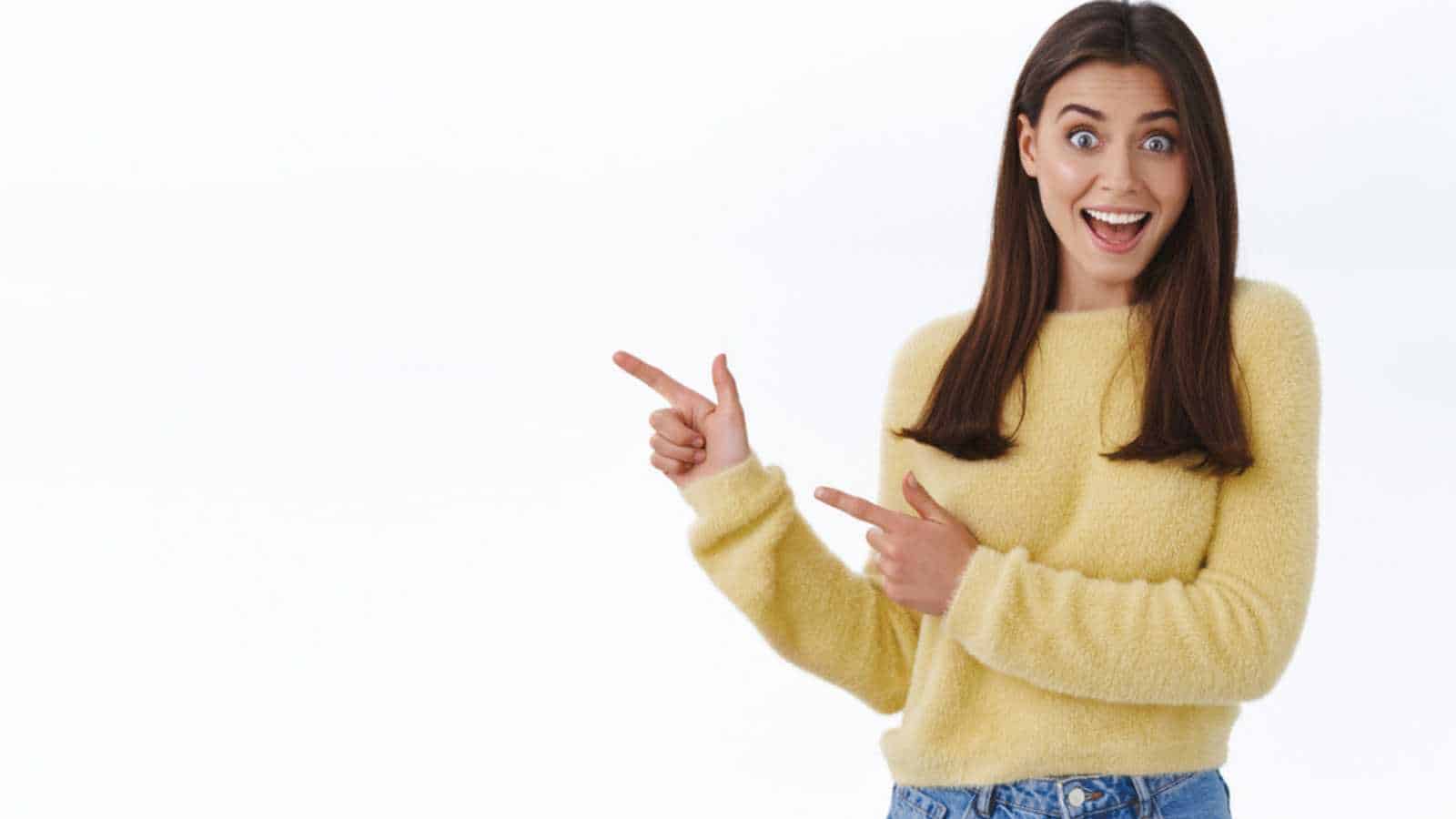Great news hey take look. Excited happy and surprised beautiful young woman in yellow sweater turn yout attention at banner, pointing fingers left and scream joyful, stand white background