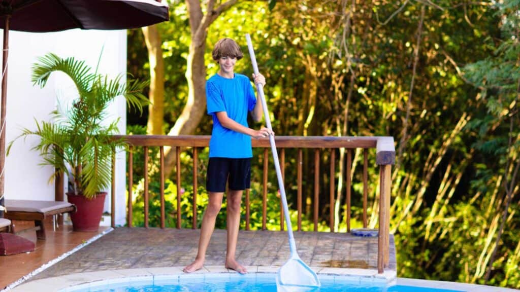 Boy cleaning swimming pool. Maintenance and service for outdoor pool. Teenager after school job and house help. Teen student picking foliage leaf out of water. Garden and backyard chores.